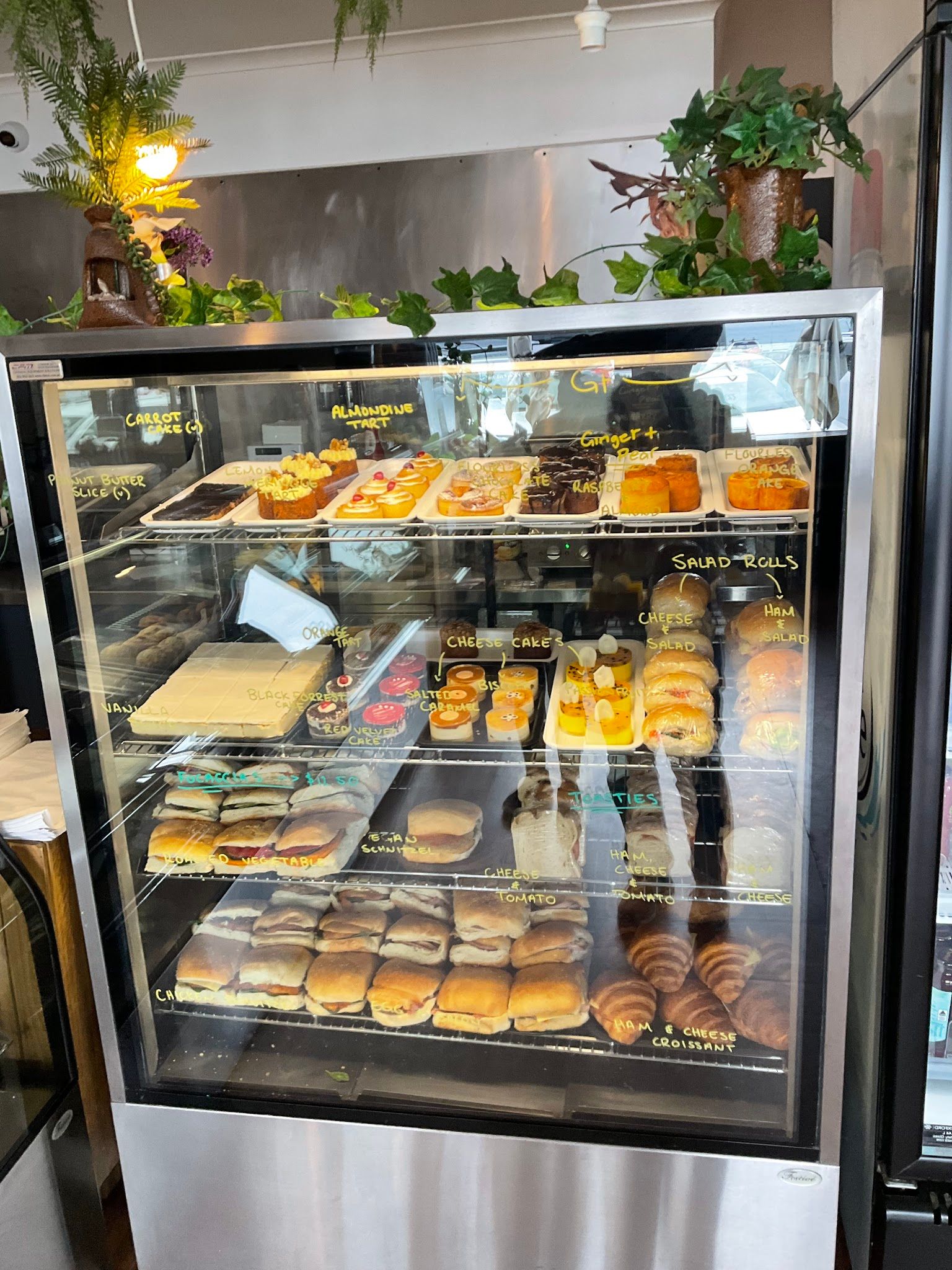 Glass display cabinet full of pastries and rolls with chalk labels and hanging greenery