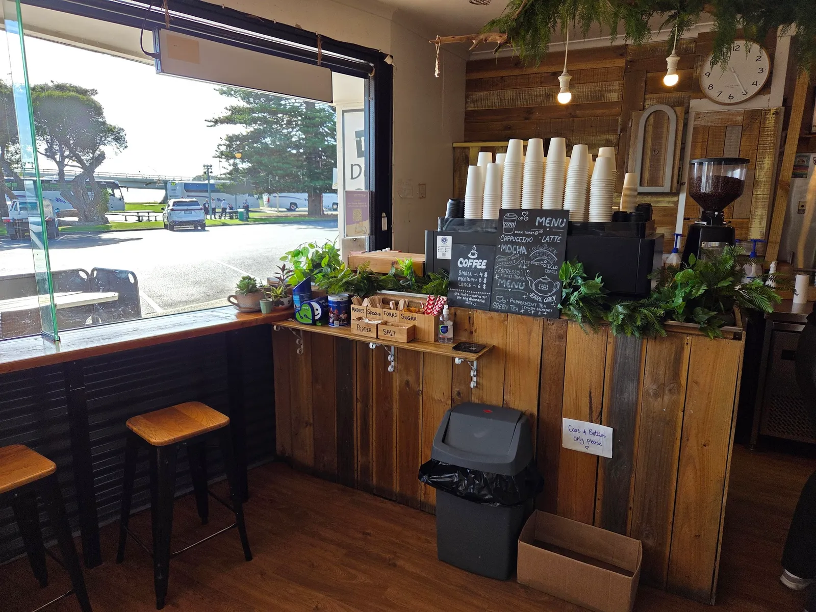 Timber coffee counter with takeaway cups, chalk menu and stools beside a window