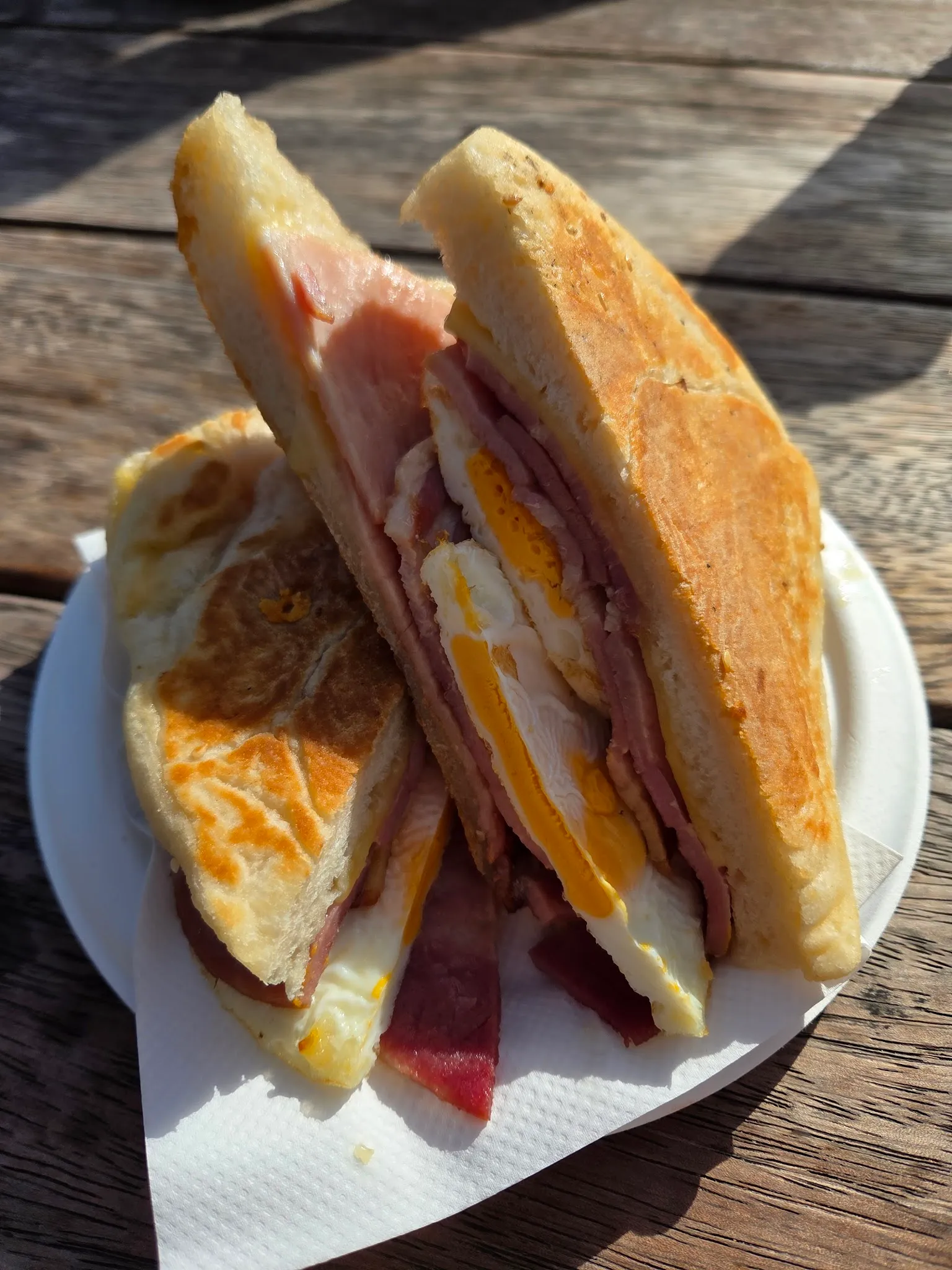Toasted ham, egg and cheese melt cut in half on a plate on a sunny timber table