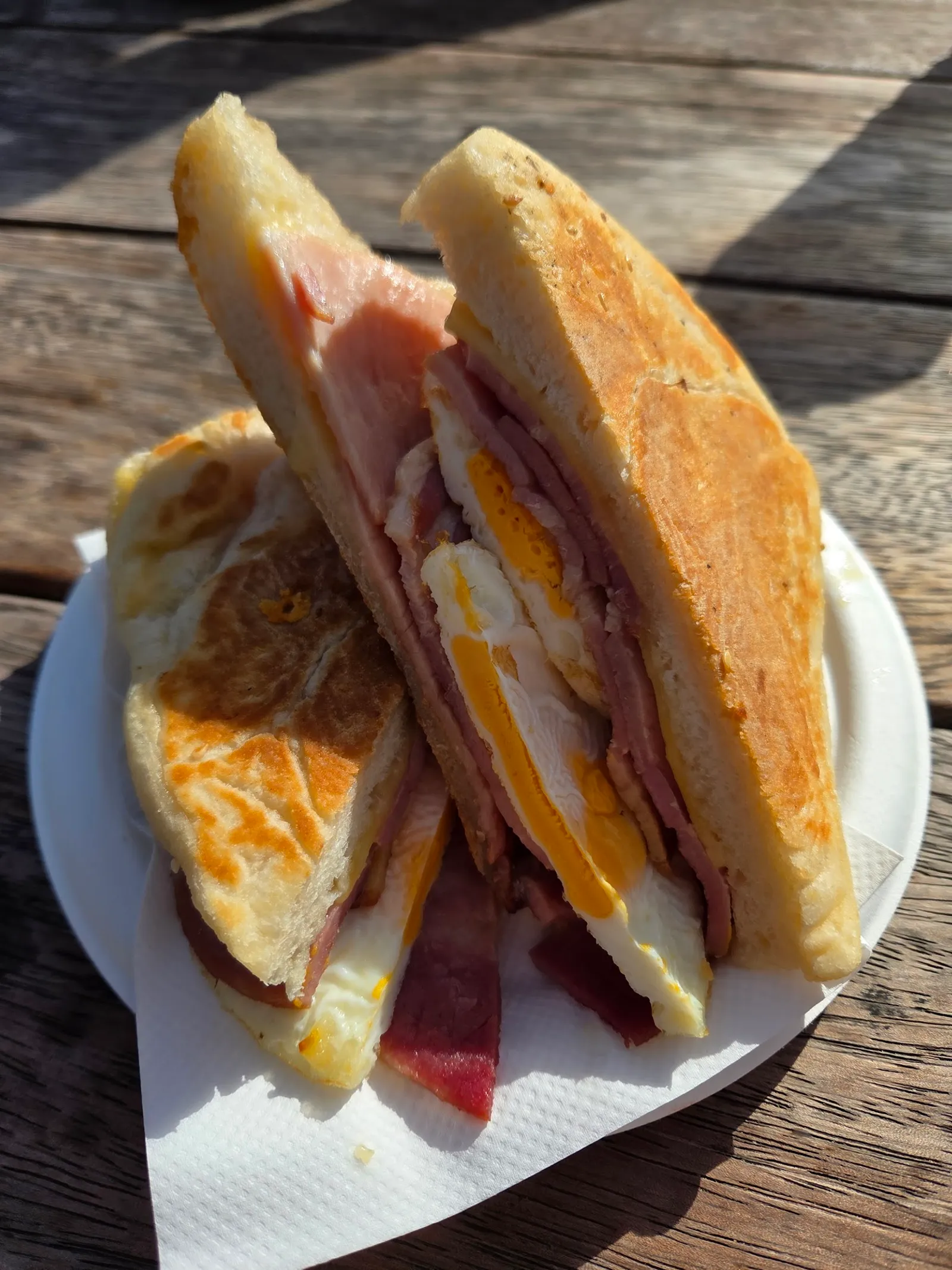Toasted ham, egg and cheese melt cut in half on a plate on a sunny timber table