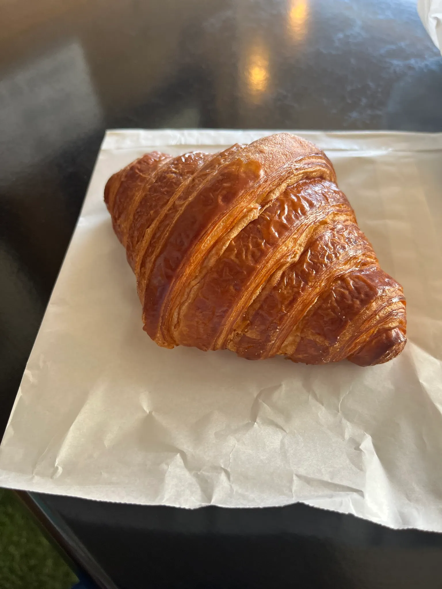Glossy laminated butter croissant on white paper on a dark table