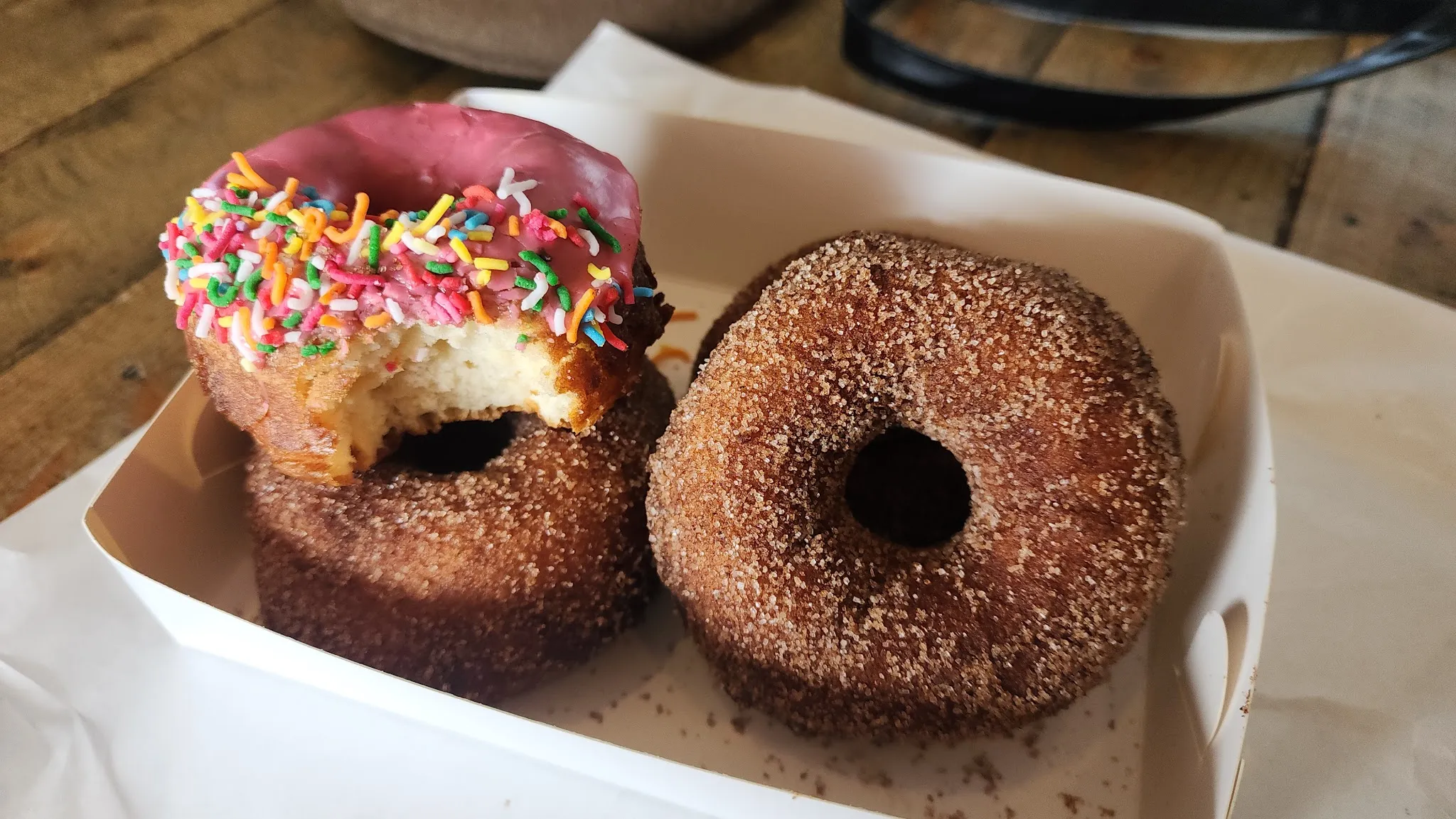 Pink-iced sprinkle donut and two cinnamon sugar donuts in a takeaway box
