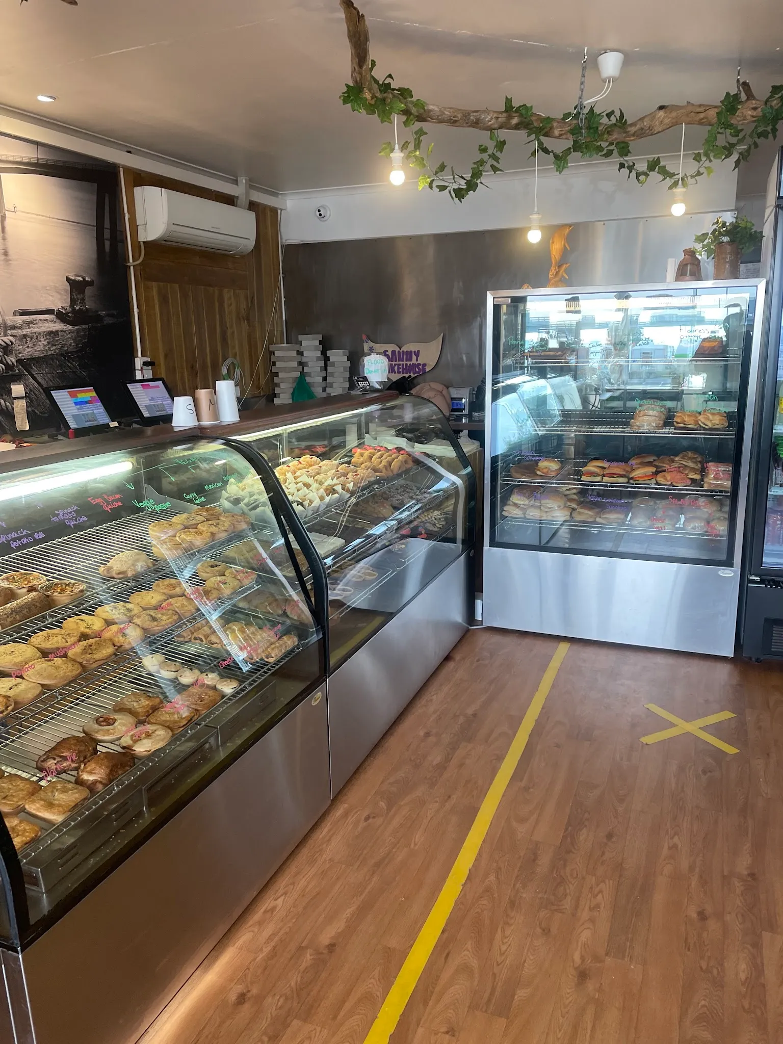 Two lit glass cabinets full of pastries and cakes inside the bakery with timber floors