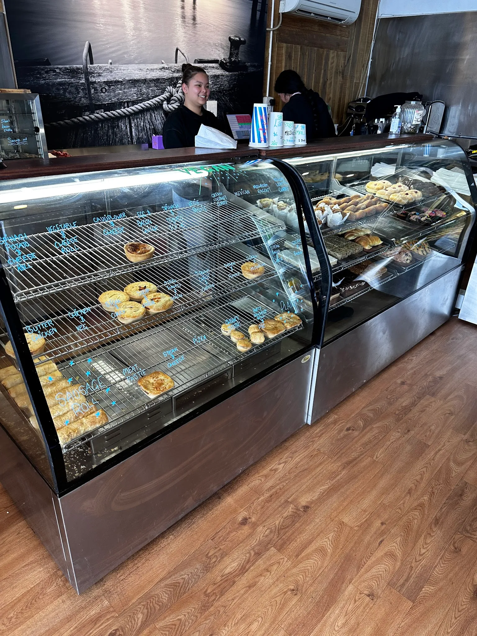 Smiling staff member behind a long glass pastry cabinet with a seascape mural